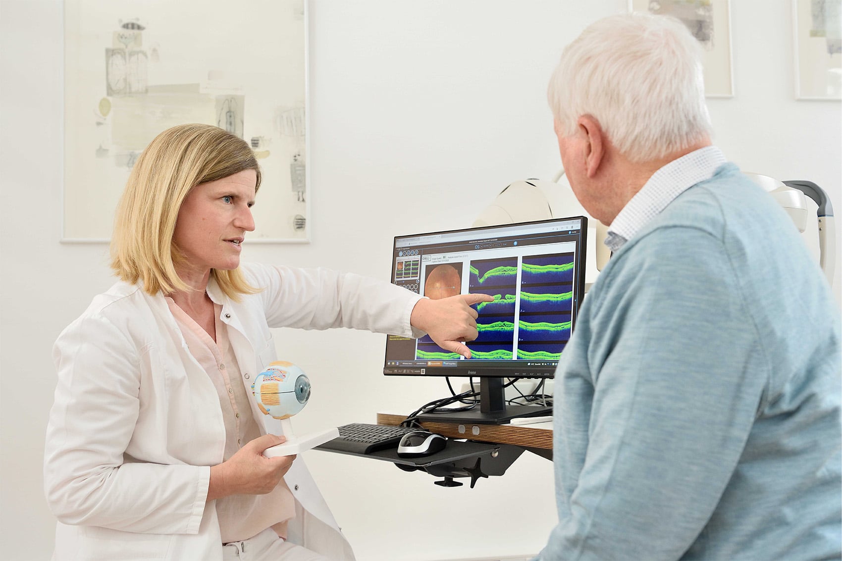 Zwei Mediziner in OP-Kleidung und mit Mundschutz bereiten einen Patienten in einem modernen Operationssaal auf einen Eingriff vor, wobei im Hintergrund medizinische Geräte und ein Monitor zu sehen sind.